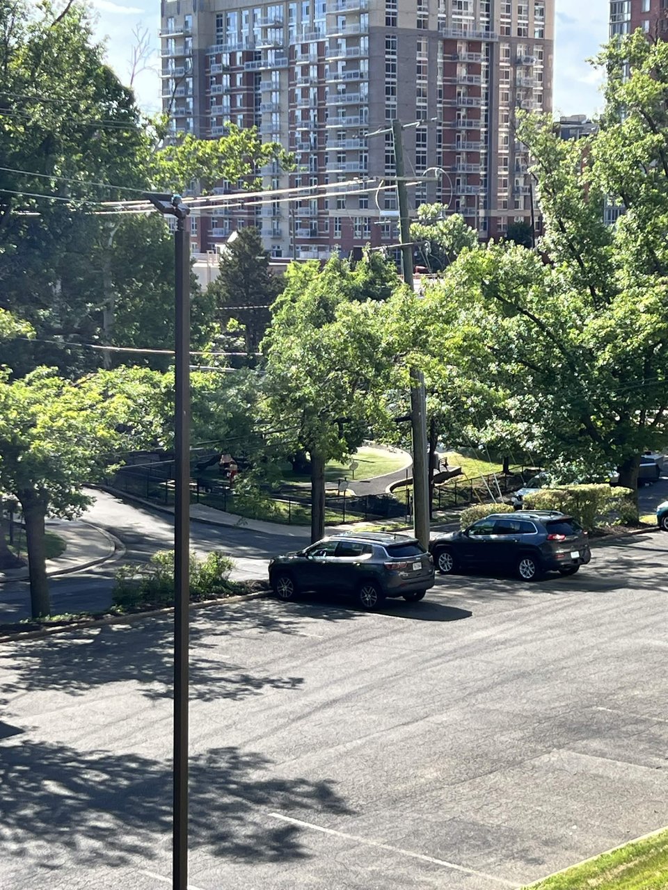 A view of a small parking lot and playground shot from high on a hill across the street. Its late in the day, the shadows are long.