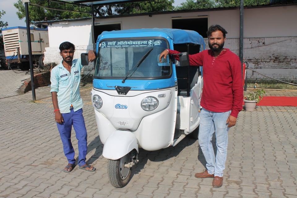 Two technicians stand next to an electric autorickshaw