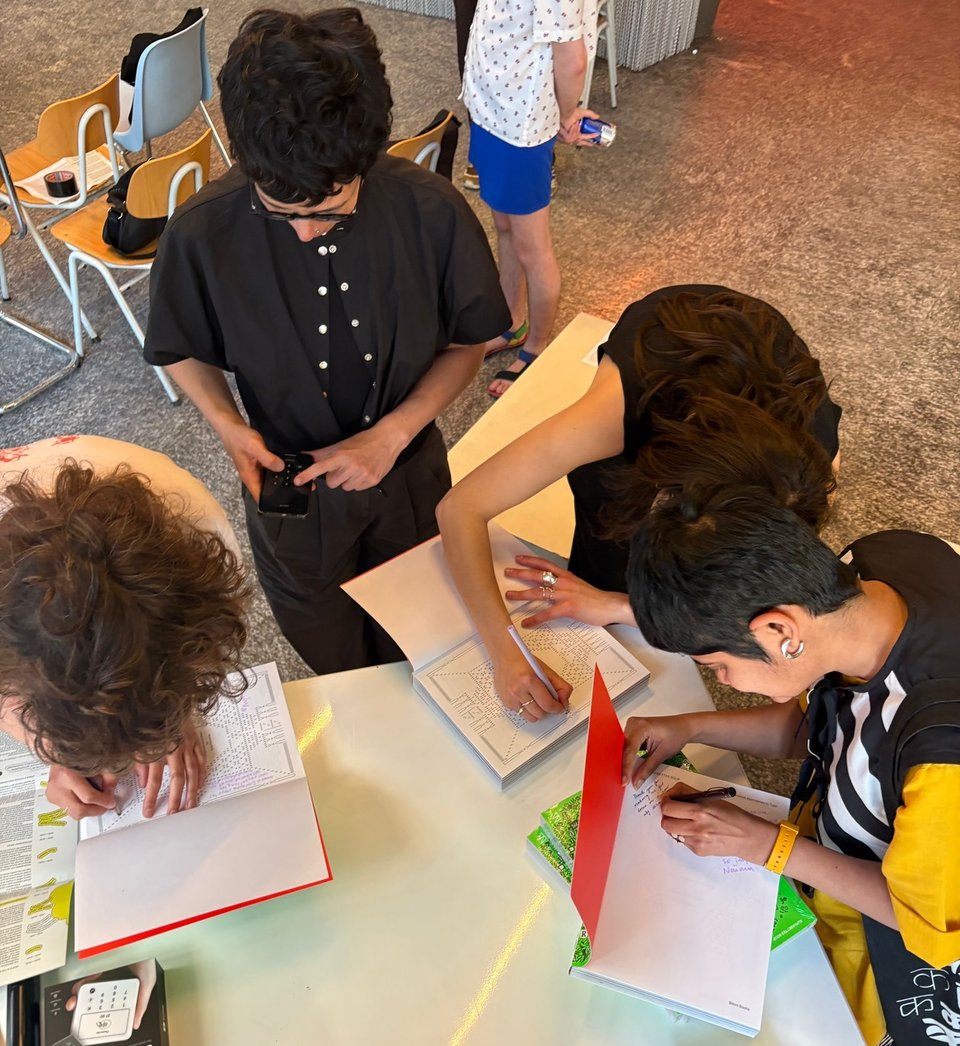 people standing and sitting at a table signing and writing in tcopies of a book