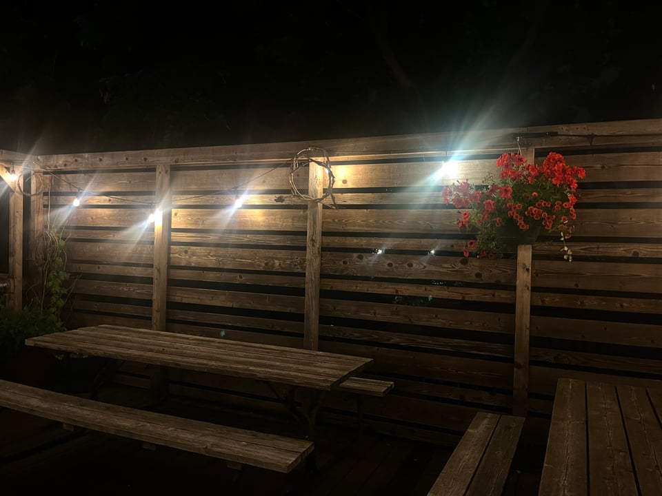 Bur Oak deck at night with bright fairy lights and a hanging basket of red flowers against the wood