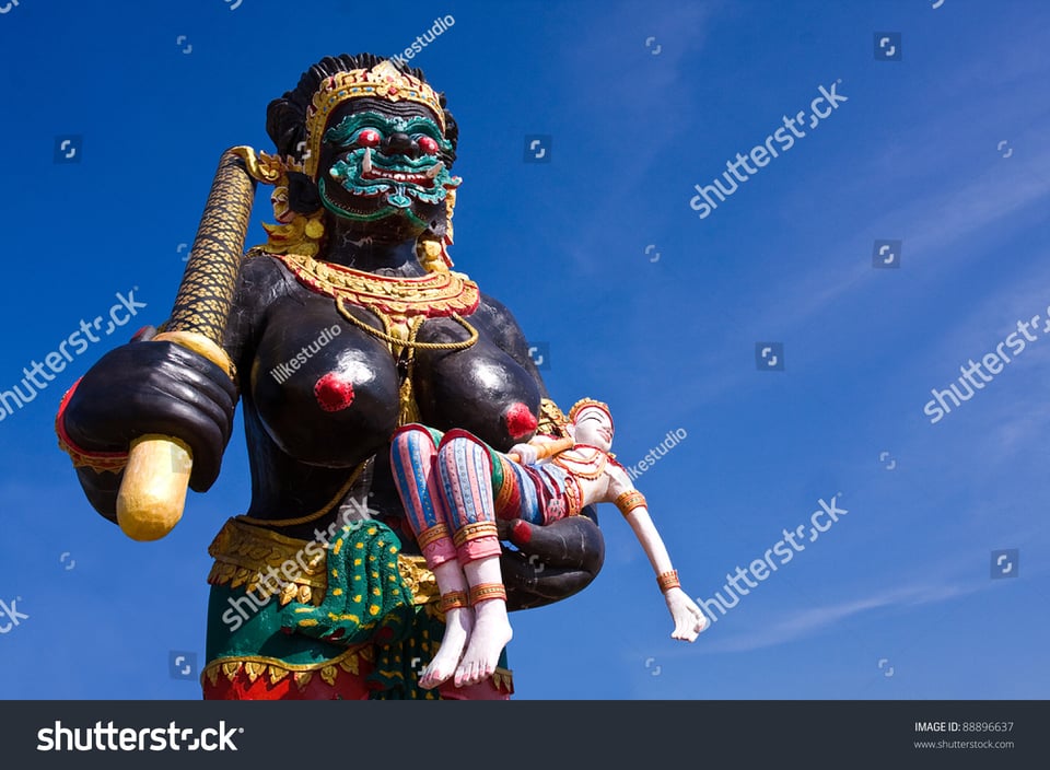 A huge black-skinned demon holds a baton in one hand and a pale little prince in the other, nestling him under one enormous exposed and red-tipped breast.