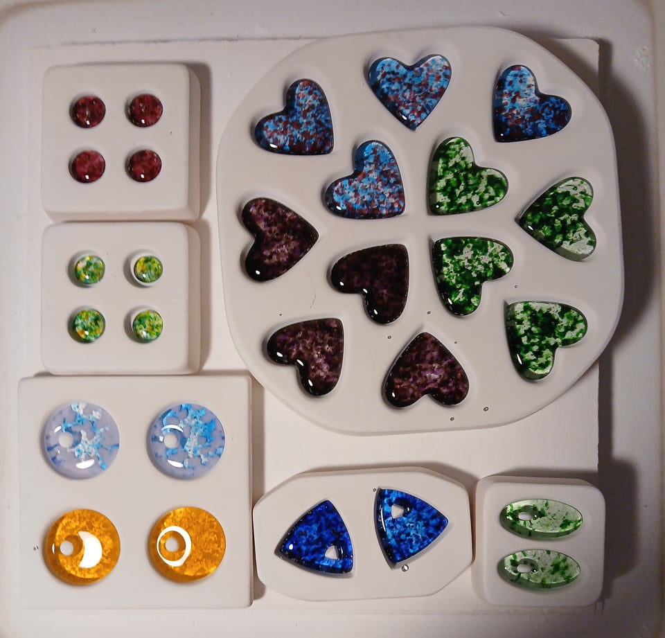 the glass in the molds has melted and you can see the colors, a very vibrant and saturated mix of red circles, mossy green circles, bigger pendant circles in blue/pink and yellow, blue triangles, mossy green ovals, and hearts in blue/pink, purple and mossy green