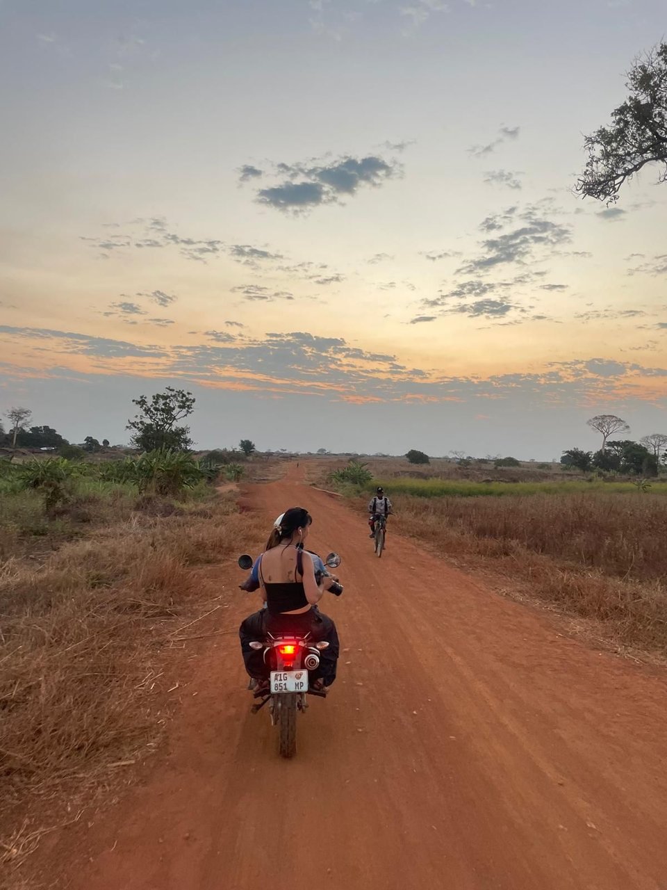 I ride pillion on a bike through a countryside landscape, camera in one hand.