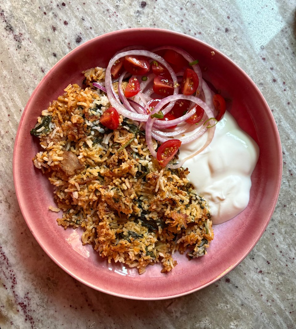 Wali ya mboga, or rice and vegetables, alongside a kachumber salad of red onions and tomatoes with a salted yogurt sauce alongside on a pink plate.