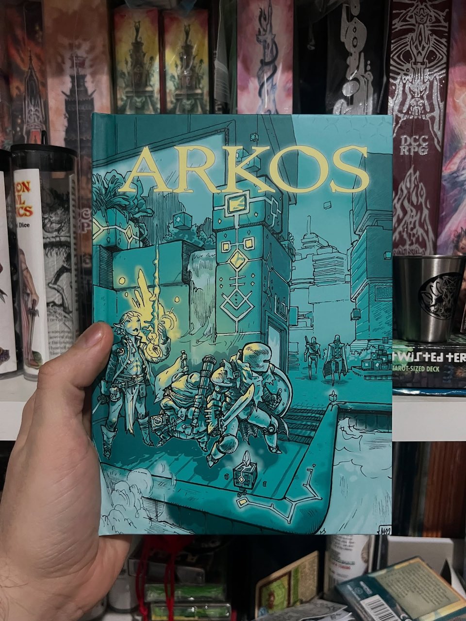 cover of a hardback book all in greens and yellows, depicting a group of adventurers turning the corner on a scifi fantasy city. robot guards are looking for them in the background.