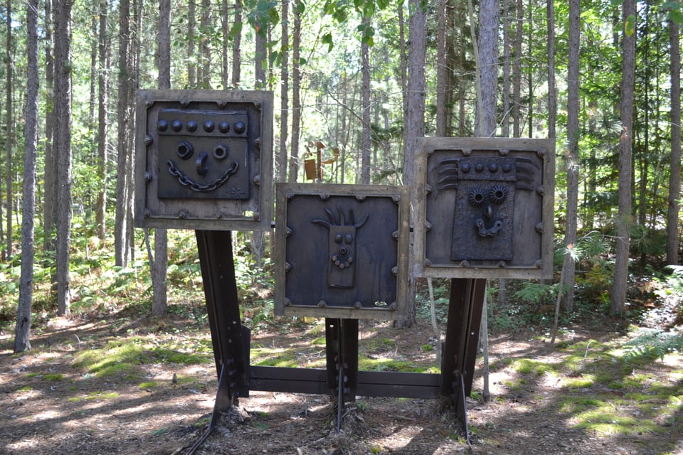 A sculpture of three square plates on an iron frame, each marked with a different robotic face.