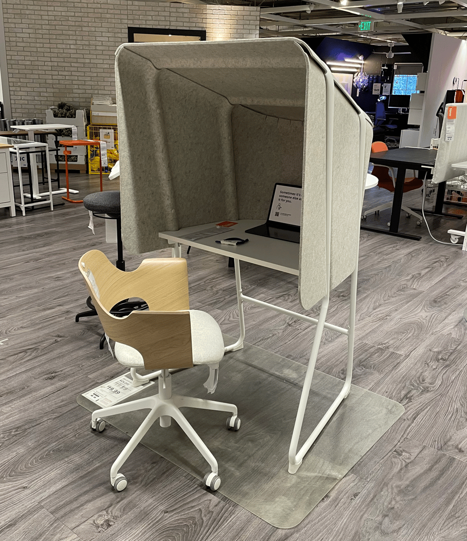 A picture of a desk at Ikea. It has a chair and a large hood over the desk for privacy