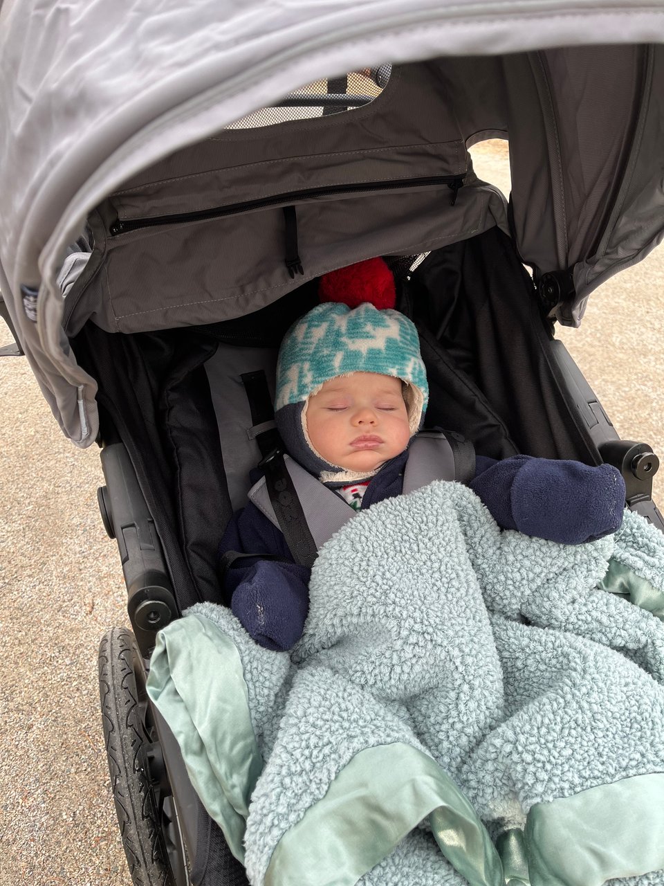 A baby bundled up in a fleece onesie and blanket napping in a stroller