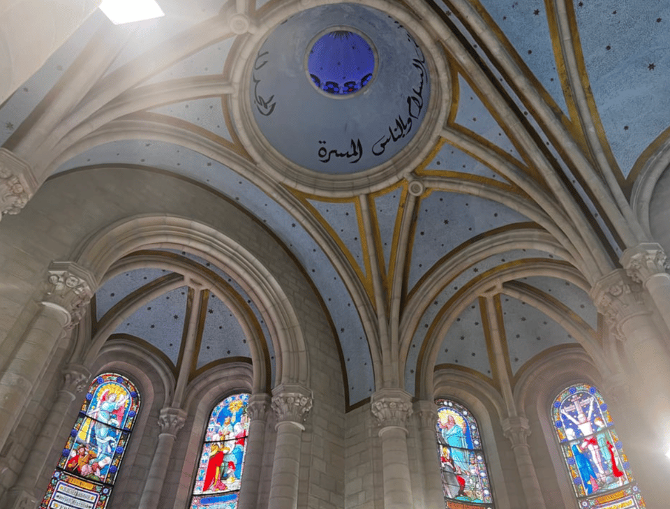 A vaulted church ceiling with a dome containing writing in Arabic, and below that, stained glass windows