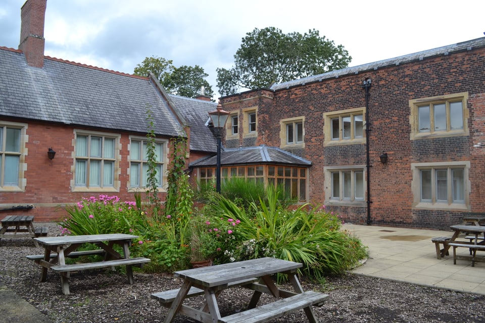 A brick building with slate roofs and stone window frames around a courtyard with picnic tables.