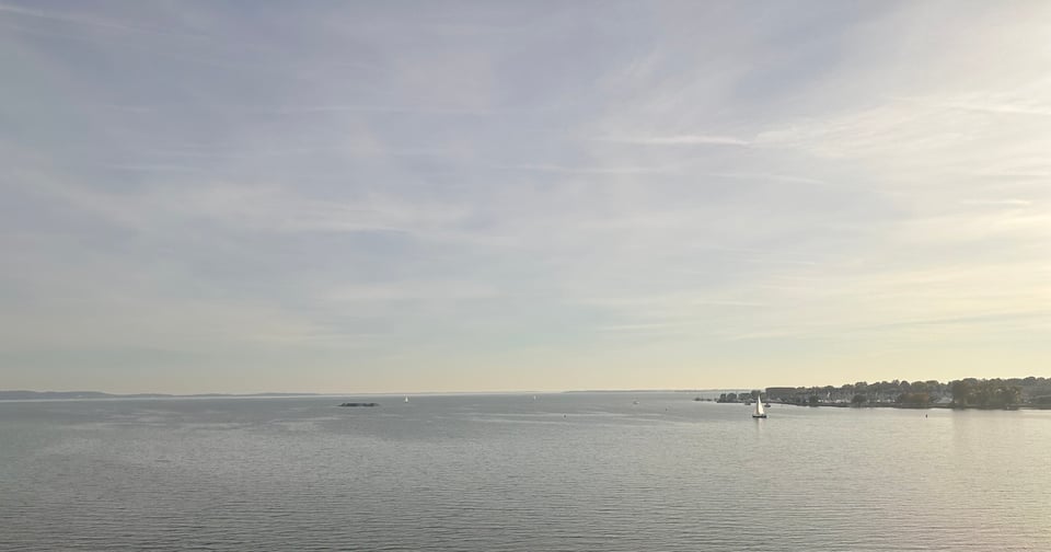view from a train window of water and a sailboat in the distance