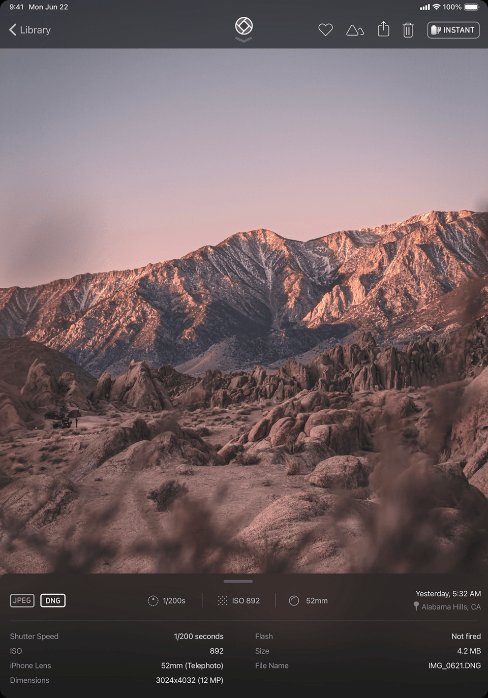 A screenshot of the iPhone app "Halide". it shows the app being used to take a picture of a mountain far in the background. The mountain is brown and black and lit, quite dramatically, by a sun that is rising offscreen to the left. At the top and bottom of the image show the various controls in the photo app.