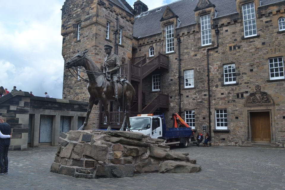 A bronze equestrian statue in front of a stone house with numerous square windows with lead panes.