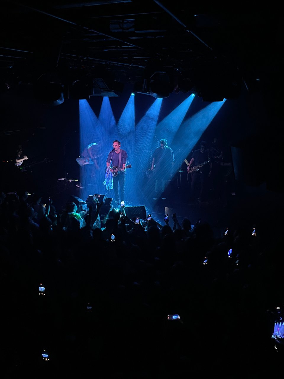 The singer of the band "No Te Va Gustar" stands in front of an energetic crowd. He is bathed in blue light from six lights creating a beautiful effect on stage.