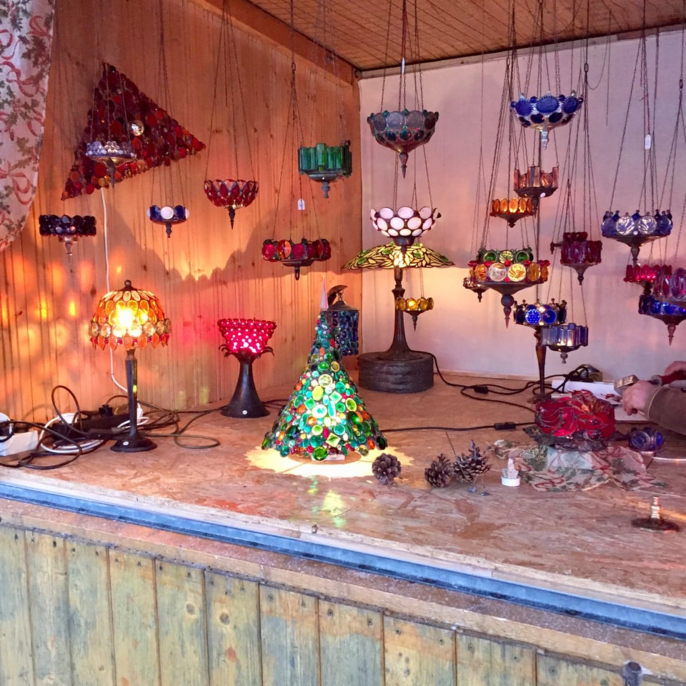 A market stall in Vienna displaying illuminated glass in various shapes. There's a Christmas tree, several hanging lights in different colours, and some glowing table lamps too. Image by Rowan Ambrose.