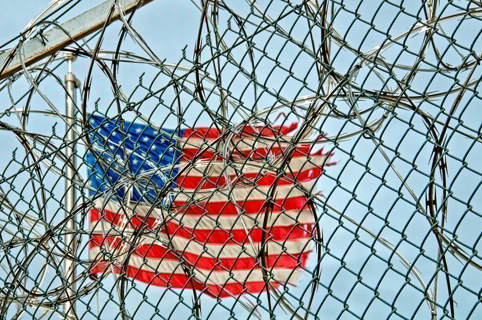 US flag seen through a barbwire fence
