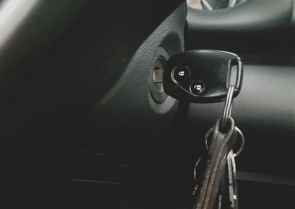 A close up of car keys stuck into the ignition, a bunch of other keys and key chains hanging from it.