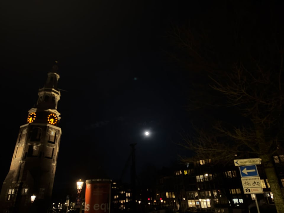 The full moon shines in the middle of a dark skyline over Amsterdam.