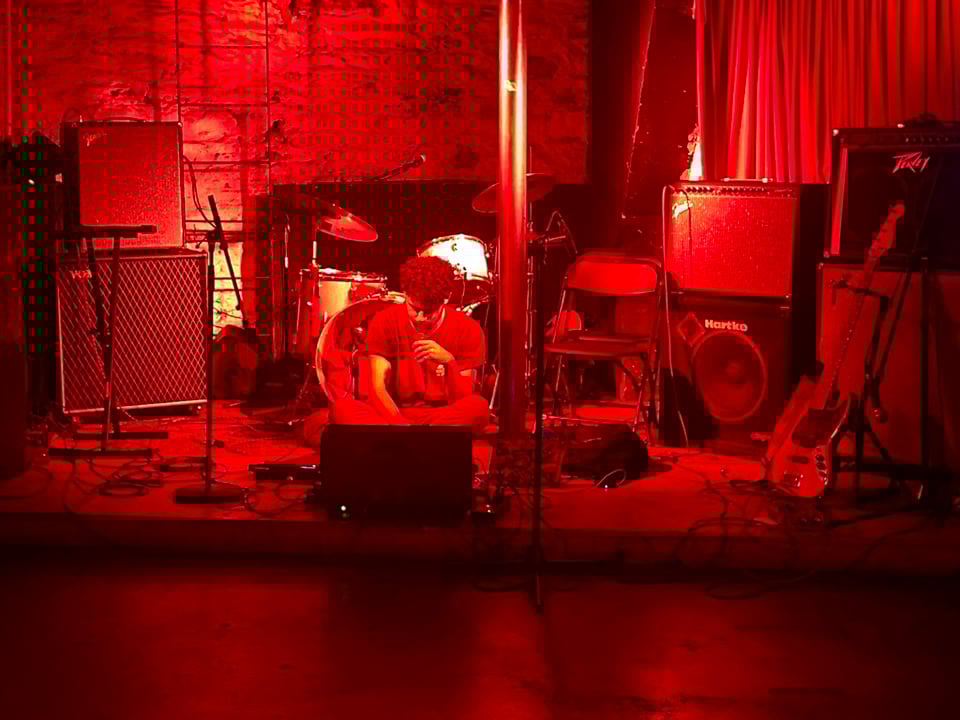 me performing while sitting cross-legged on a stage, cloaked in red light.