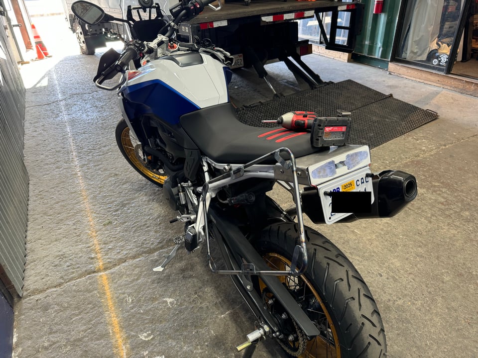 A motorcycle with a pannier (luggage) rack mocked up on the left side, seen from the back.