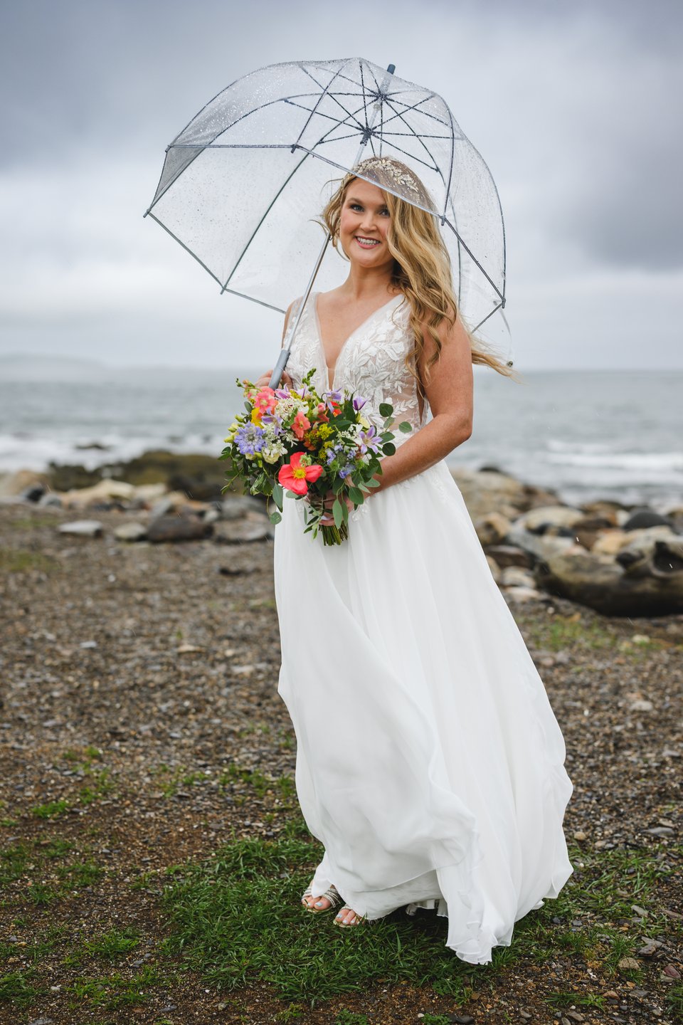Bridal portrait of a bride looking happy and excited holding an umbrella and her bouquet with the sotrmy ocean behind her