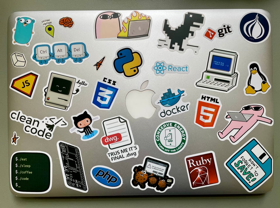 Top down view of the old macbook air covered with said cheap stickers. There are stickers like 'Don't forget to save' and 'Trust me it's final.dwg' and such. Feel free to laugh