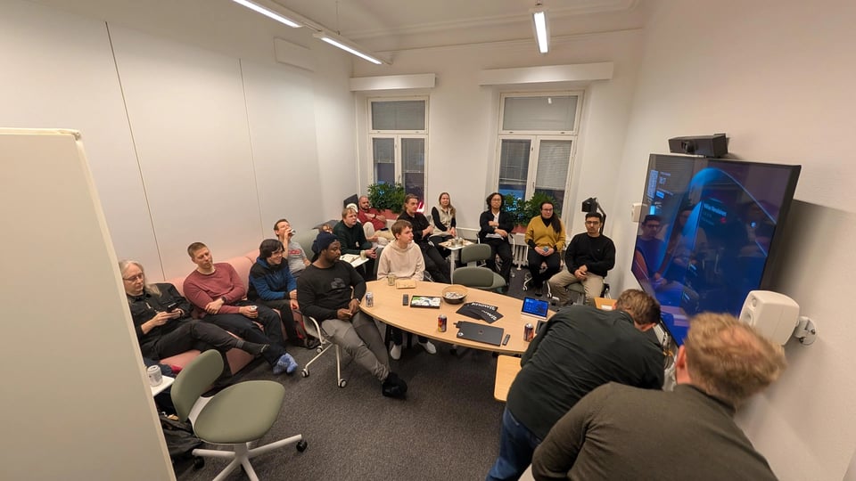 A meeting room full of people watching at a TV in the room as it's being setup for a presentation