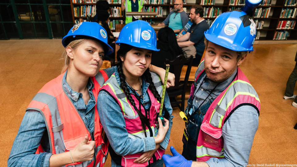 Three people in hard hats and high visibility vests pose for the camera in a library.