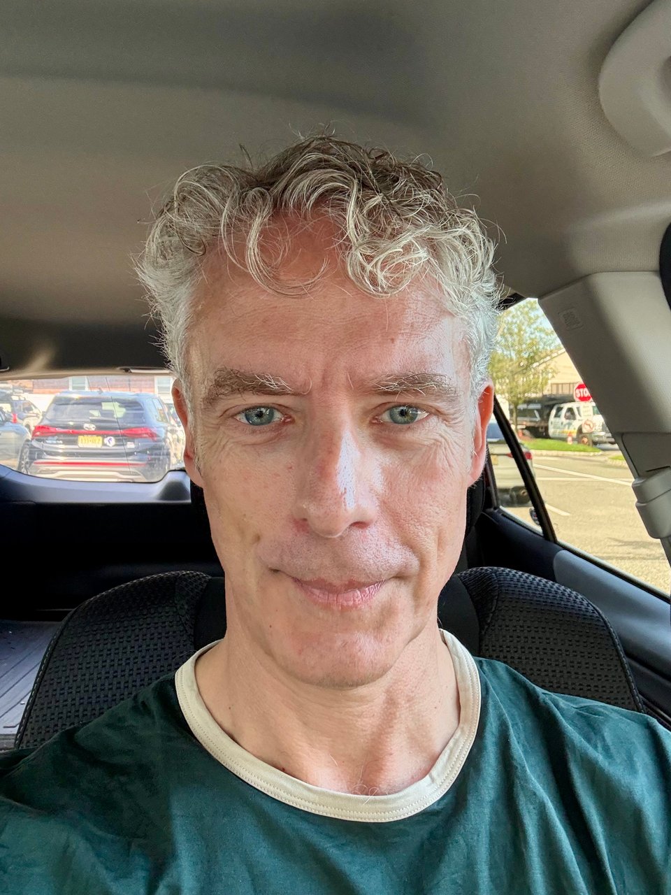 selfie of white man inside parked car; he's wearing a hunter-green ringer T-shirt with a beige collar, and is smiling with his mouth shut