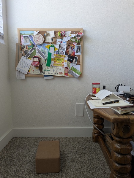 A cork yoga block on the floor faces the short edge of a wooden coffee table, where paper and notebooks and a fountain pen are strewn about.