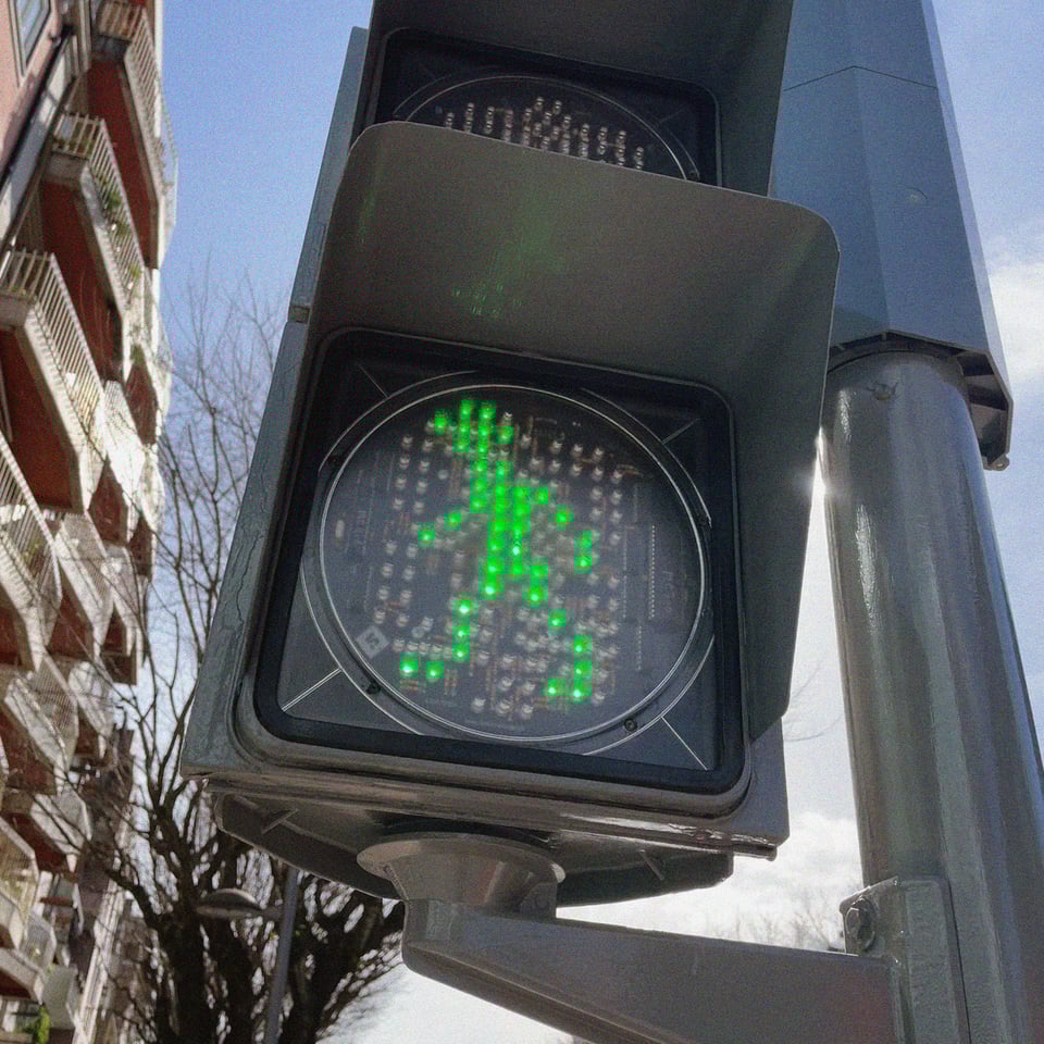 the green walking man animation from the crosswalk signs in Portugal against a brilliant blue day and an apartment building