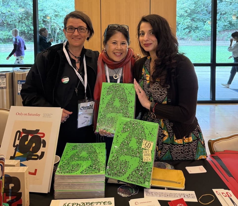 Three people stand smiling in front of books and other printed materials
