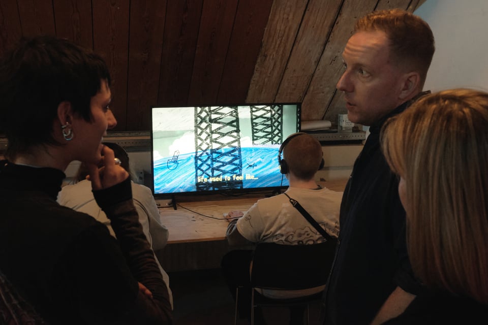 A group of people chat in front of a computer screen where a person is playing