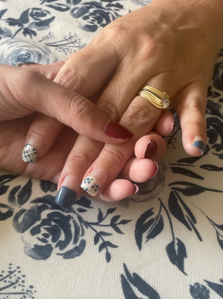 Two hands holding each other. One hand has grown out blue and white patterned painted nails.