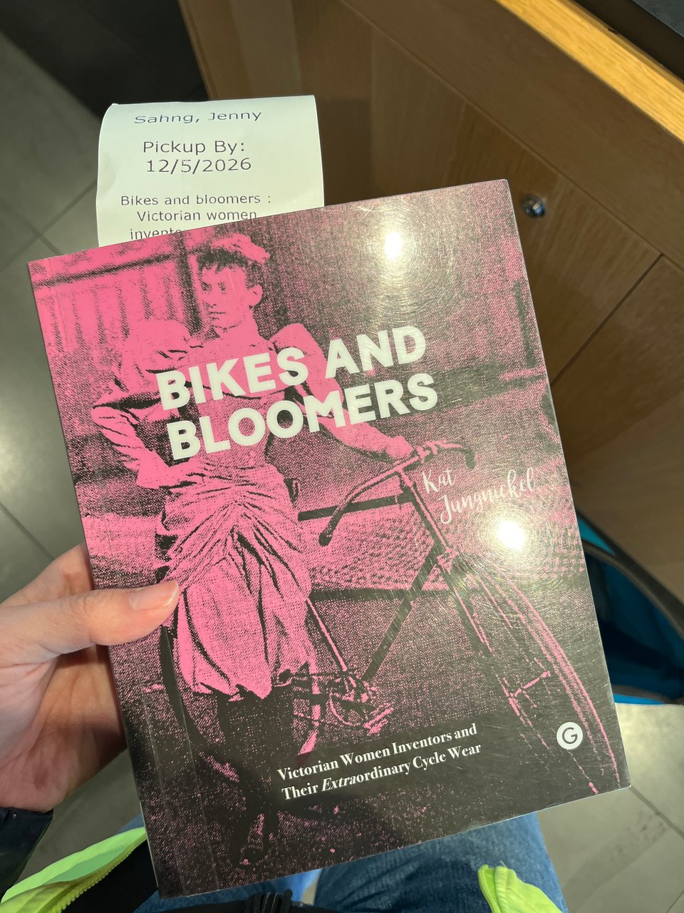A book called "Bikes and Bloomers: Victorian Women Inventors and their Extraordinary cyclewear" featuring an old photo of a woman in a corset and puffy sleeves, wearing an interesting ruched pair of skirt/pants next to a bike.