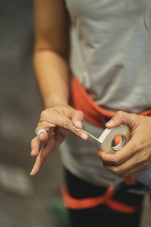 Close up on the hands of a person doing construction, they are holding a small white roll of masking tape and a segment of tape away from the roll