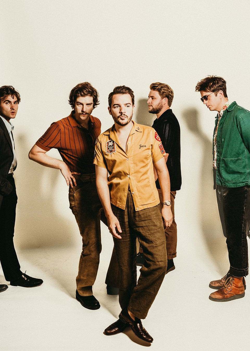 A group of five men in the band LuxDeluxe stand together, one of them in the center slightly in front of the other four.