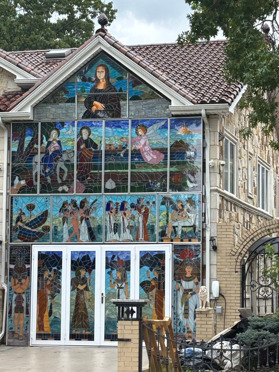 This two story beige brick building has completely replaced the entire face of their house - including the fronts of the doors and windows - with a bright mosaic of scenes from Egyptian and Renaissance art history, with the Mona Lisa at the top.