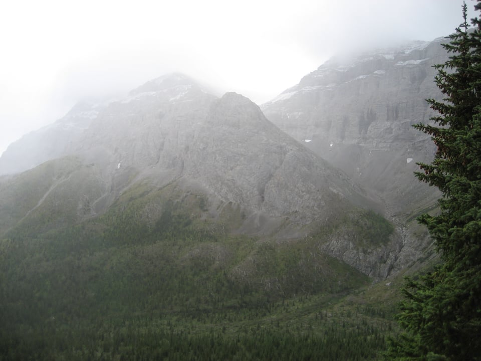 Steep rocky mountains, streaked with snow, with clouds resting on their top.