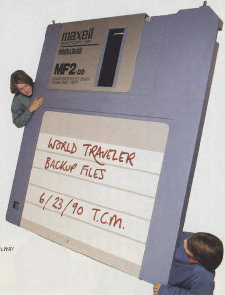 Two teenage boys are standing and laying behind a 6-foot tall model of a 3.5" Maxell floppy disk.