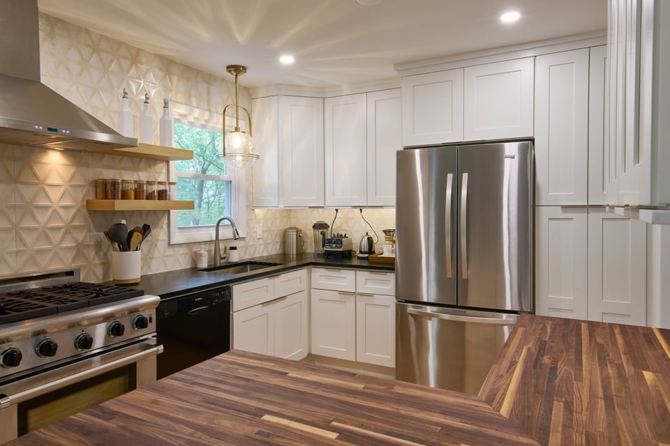 Photo of a newly renovated kitchen, with a butcher-block counter in the foreground, and a dark soapstone counter in the far corner