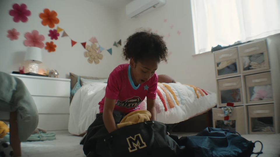 A kid from a Mazda commercial, in her bed room festooned with IKEA furniture. She's wearing a jersey/shirsey for a football team called the Valkyries.