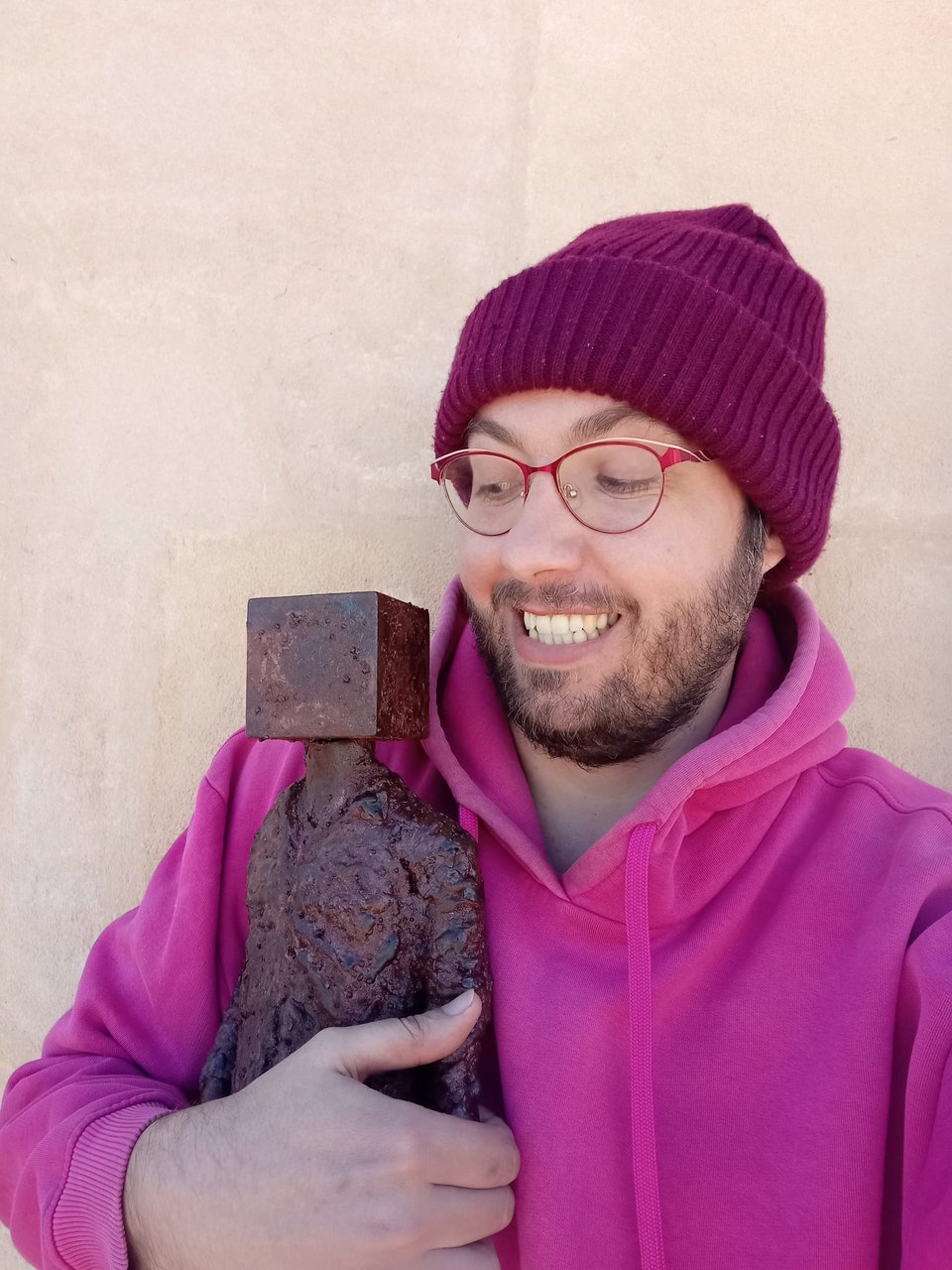 A picture of me in a pink hoodie holding a massive steel sculpture of Timothee and looking at it with a big smile