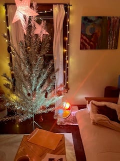 a cozy Christmas living room scene, with an aluminum tree, hanging star lamp, fairy lights, sleeping cat, and color wheel tinting everything with a red glow