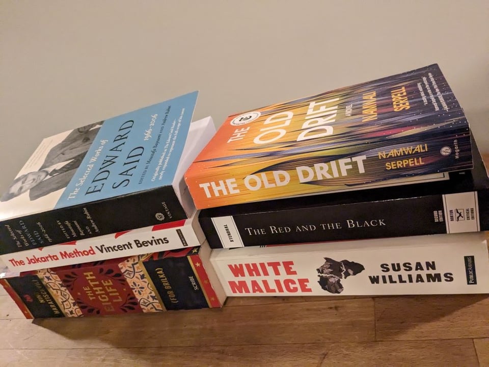 A stack of books on a table: The Selected Works of Edward Said, The Jakarta Method by Vincent Bevins, The Eighth Life by Nino Haratischwili, The Old Drift by Namwali Serpell, The Red and the Black by Stendhal, and White Malice by Susan Williams.