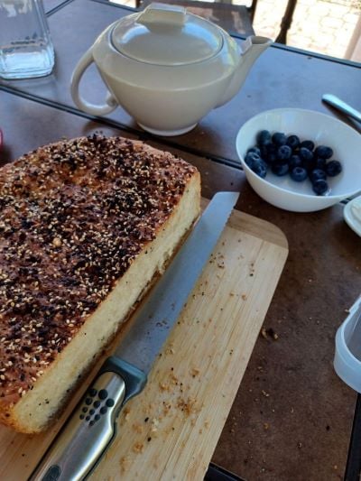 An outdoor table set for a tea party, with a loaf of bread, a bowl of blueberries, and of course a pot of tea
