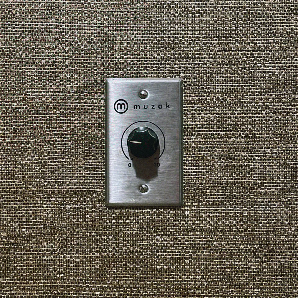 a knob that reads "muzak" and goes from 0 to 10 on a burlap-textured wall in a out-of-date but very sweet hotel