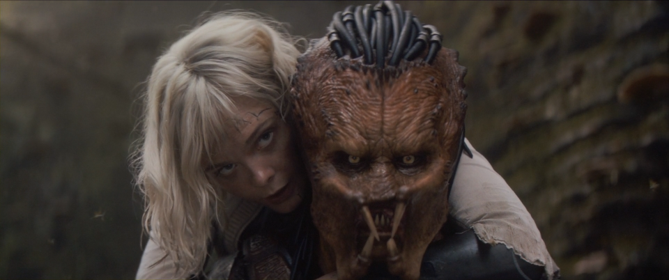 A still from Predator: Badlands where Dek is carrying Thia on his back, both of them facing forward.