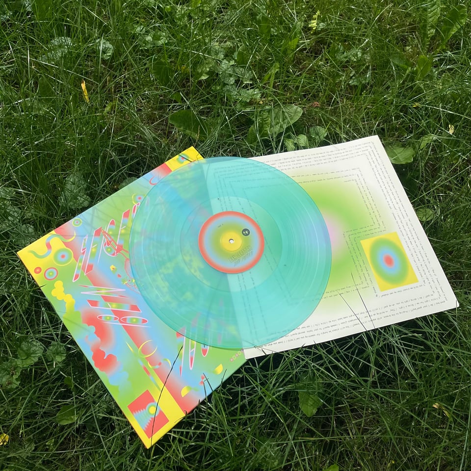 a icy blue vinyl record copy of Youth Pastoral pulled out of its sleeve sits on a lawn of overgrown grass