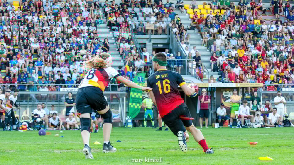 a Germany chaser guards a Belgium keeper in front of a crowd of 2,000 fans in a football stadium during the finals of the quadball world championship